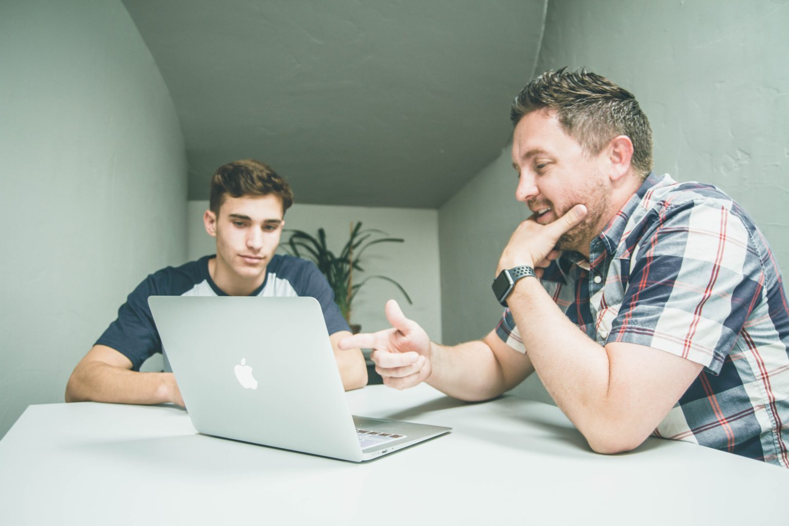 a couple of men sitting at a table with a laptop and a cell phone