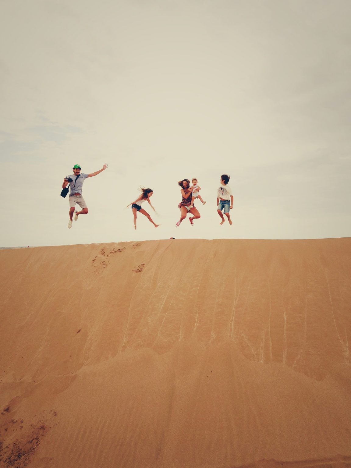 a group of people jumping on a sand dune